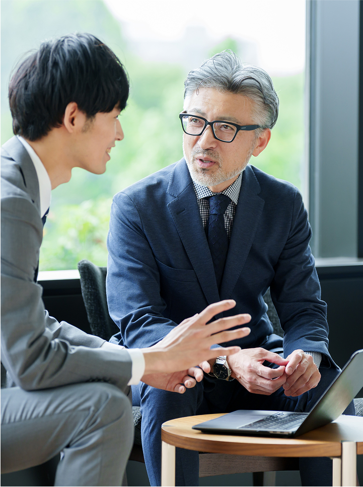 年配の男性が話を聞きながら意見を交わす、落ち着いた雰囲気の対話場面