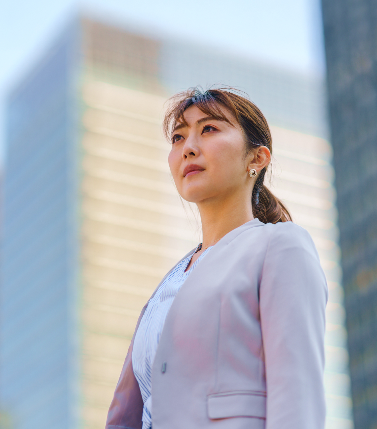 高層ビルを背景にスーツ姿で前を見つめる女性のポートレート
