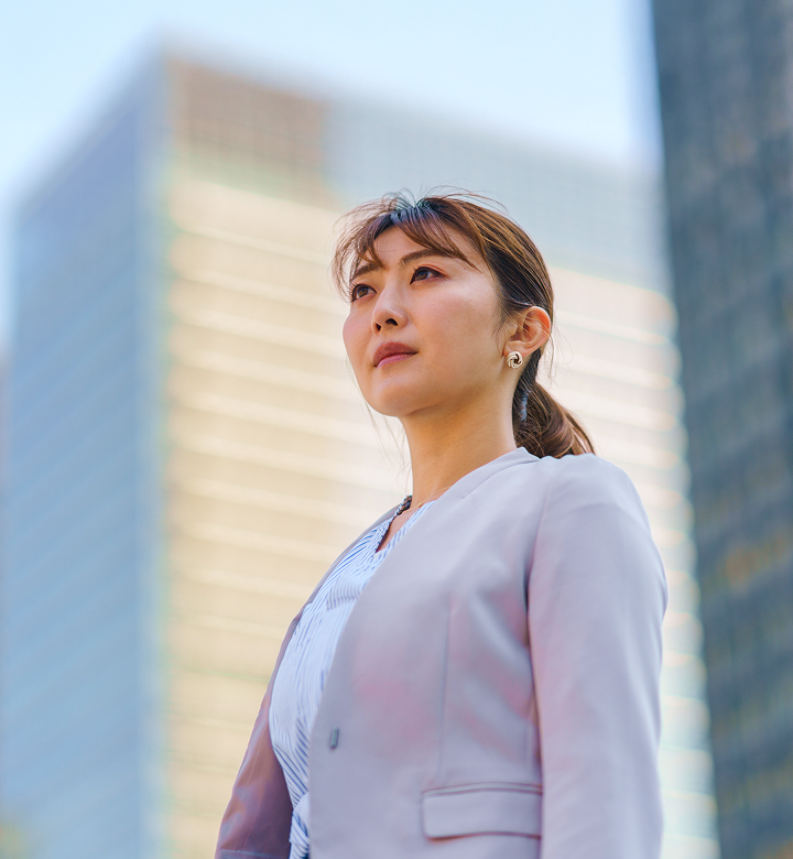 高層ビルを背景にスーツ姿で前を見つめる女性のポートレート